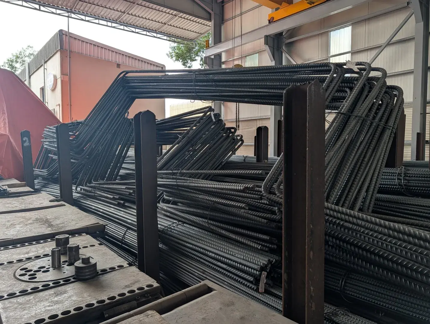 Large-diameter bent rebar bundles stored in racks beside a rebar bending table in the Global Trade House workshop